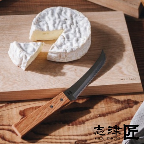 圖片中一個未切的布里起司旁，放著一塊切好的起司和一把木柄鋸齒刀，都放在榆木砧板上。
