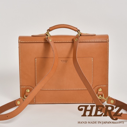 職人手作皮革極簡風三用商務公事包，淺棕色皮革，設有提把、可拆卸側背帶，以及肩背帶。包身正面有壓印品牌標誌。