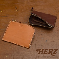 兩款職人手作皮革L型拉鍊迷你短夾，一款為淺棕色，另一款為深棕色。皆採用光滑的皮革材質，搭配金屬拉鍊和縫線，設計簡潔實用。