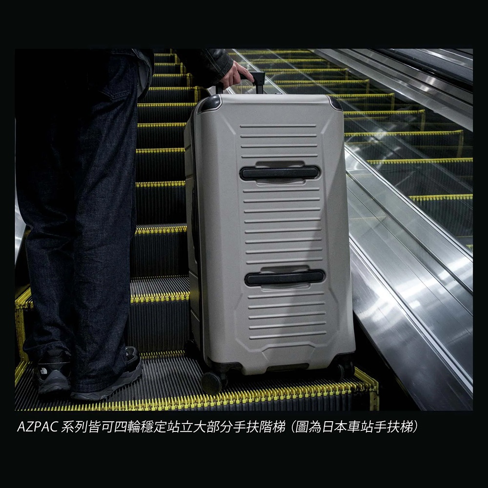 一名旅客站在手扶梯上，手持淺灰色AZPAC品牌四輪硬殼行李箱，該行李箱採用前開口設計並具有穩定站立功能，圖片下方說明文字指出該系列行李箱可四輪平穩站立於大部分手扶梯上。
