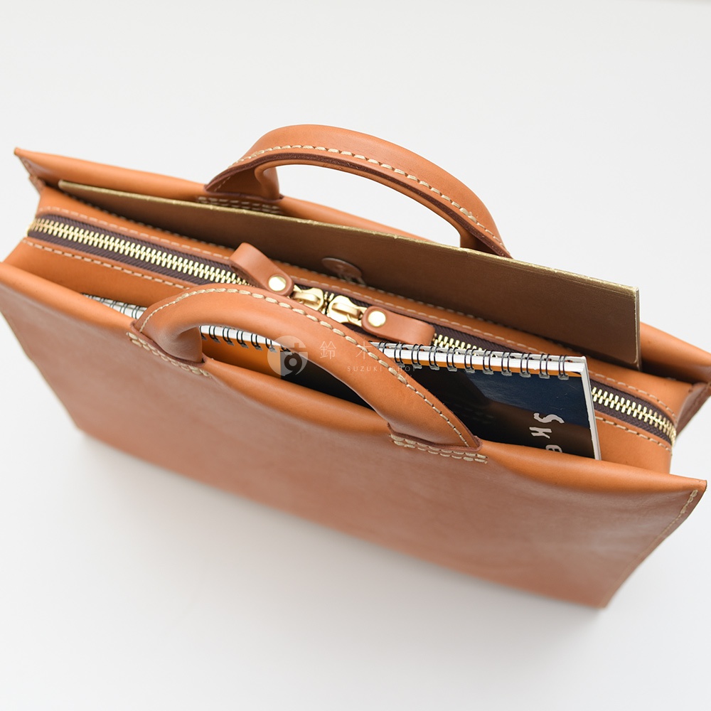 日本HERZ職人手作皮革簡約商務公事包，特寫棕色皮革包體和金色拉鍊，內部露出筆記本。