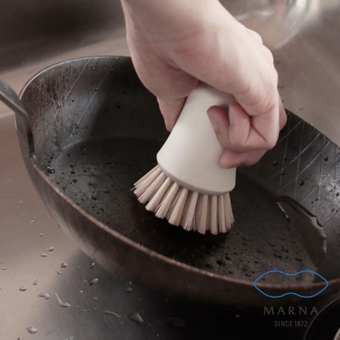 手持米白色抗菌刷毛廚房清潔刷，刷毛呈淺棕色，正清潔著一個黑色鍋具。
