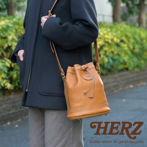 職人手作皮革束口單肩包，採用光滑的棕褐色皮革製成，束繩設計，可肩背。包身有精緻的縫線裝飾，中央有品牌壓印標誌。