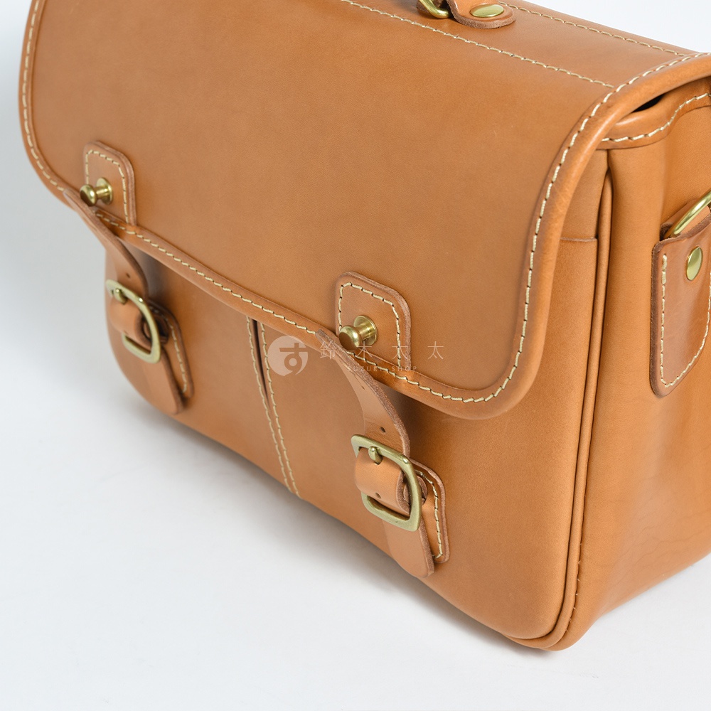 淺棕色皮革製成的雙用單肩包，飾有米色縫線及黃銅色金屬扣環，風格復古，適合商務與休閒場合。