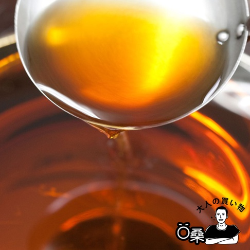 銀色金屬湯勺中盛滿琥珀色液體，一滴液體從湯勺邊緣滴落，下方是另一個裝有相同琥珀色液體的容器。