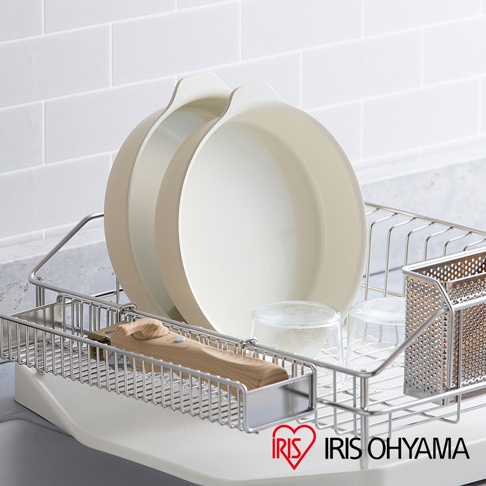 兩個淺米色圓形陶瓷不沾平底鍋堆疊在金屬瀝水架中，旁邊有兩個玻璃杯和一個木柄工具。