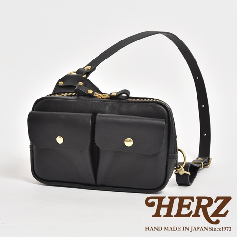 黑色皮革雙口袋斜背包，正面有兩個帶有金色鈕扣的翻蓋口袋，主袋採用金色拉鍊開合，配有可調節的皮革肩帶，整體風格簡約實用。