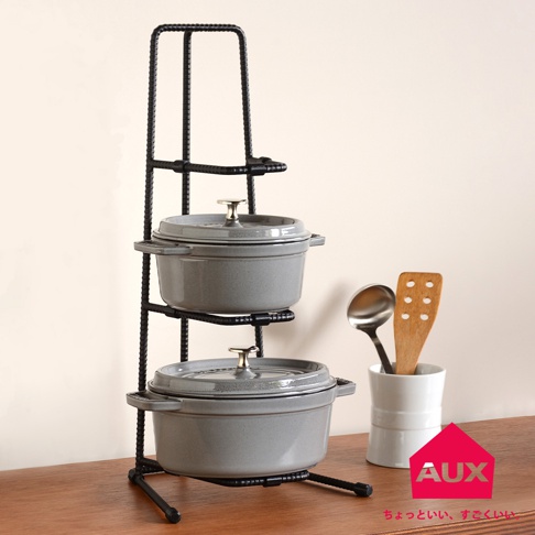 黑色金屬三層收納展示架，展示兩個灰色鑄鐵鍋，鍋蓋帶有金色把手，右側有一個白色杯子，內有湯勺和木製鍋鏟。