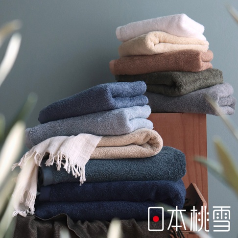 堆疊的精梳棉毛巾，顏色包含白色、米色、棕色、墨綠色、灰色、淺藍色、深藍色和藍綠色，其中一條毛巾有流蘇邊緣。