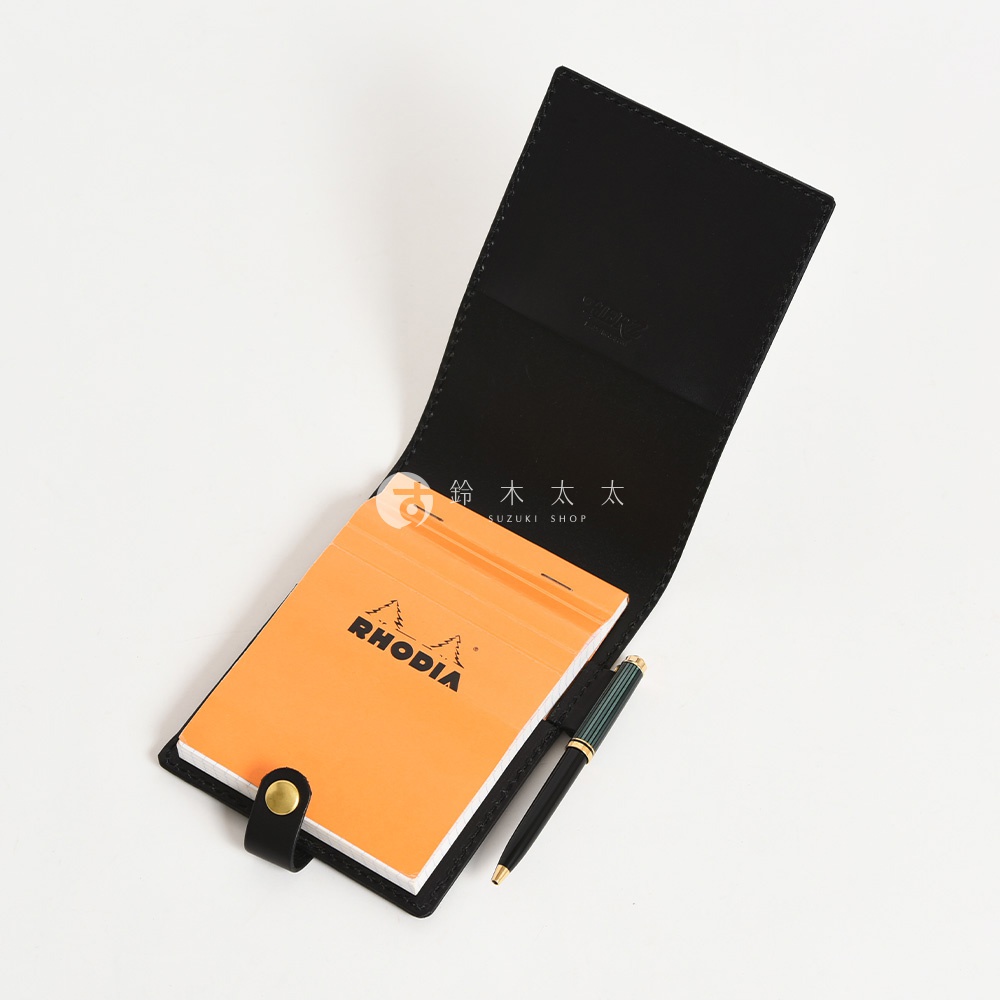 黑色皮革便利貼收納套，內含一本橘色 Rhodia 便利貼，並附有一支綠色與金色筆身鋼筆。