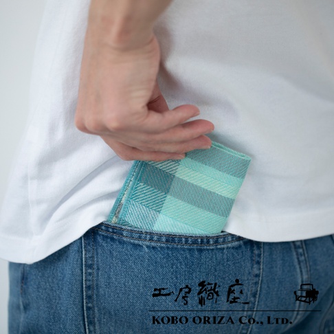 一條手臂將藍綠色格紋的信封式長方形手帕放入牛仔褲後口袋。