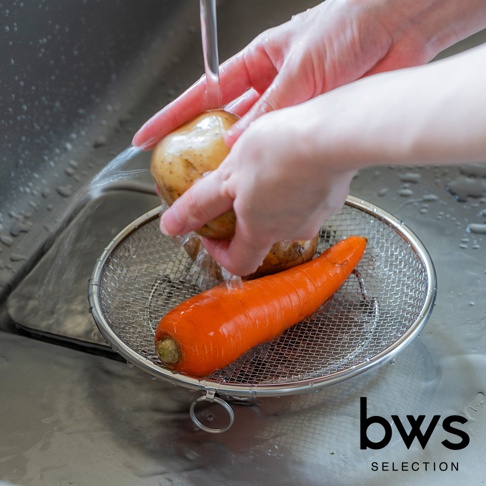 手正在水槽中清洗馬鈴薯和胡蘿蔔，下方有一個不鏽鋼瀝水籃。