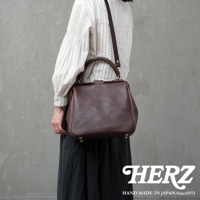 深棕色皮革製成的方形口金托特包，配有可拆卸肩帶和頂部提把，底部有金色金屬腳釘。