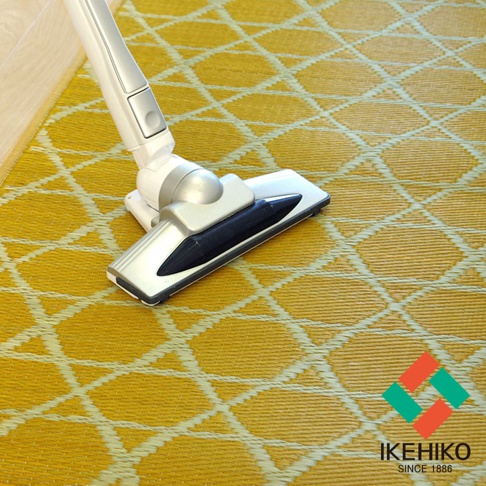 黃色榻榻米廚房地墊，織有白色菱形網格圖案，搭配銀白色及黑色吸塵器頭，在靠近地板邊緣處。