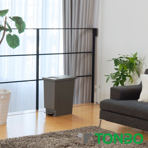 灰色30公升推蓋踩踏雙用型垃圾桶，帶有方形蓋子和底部踏板，位於房間角落，靠近窗戶和植物。