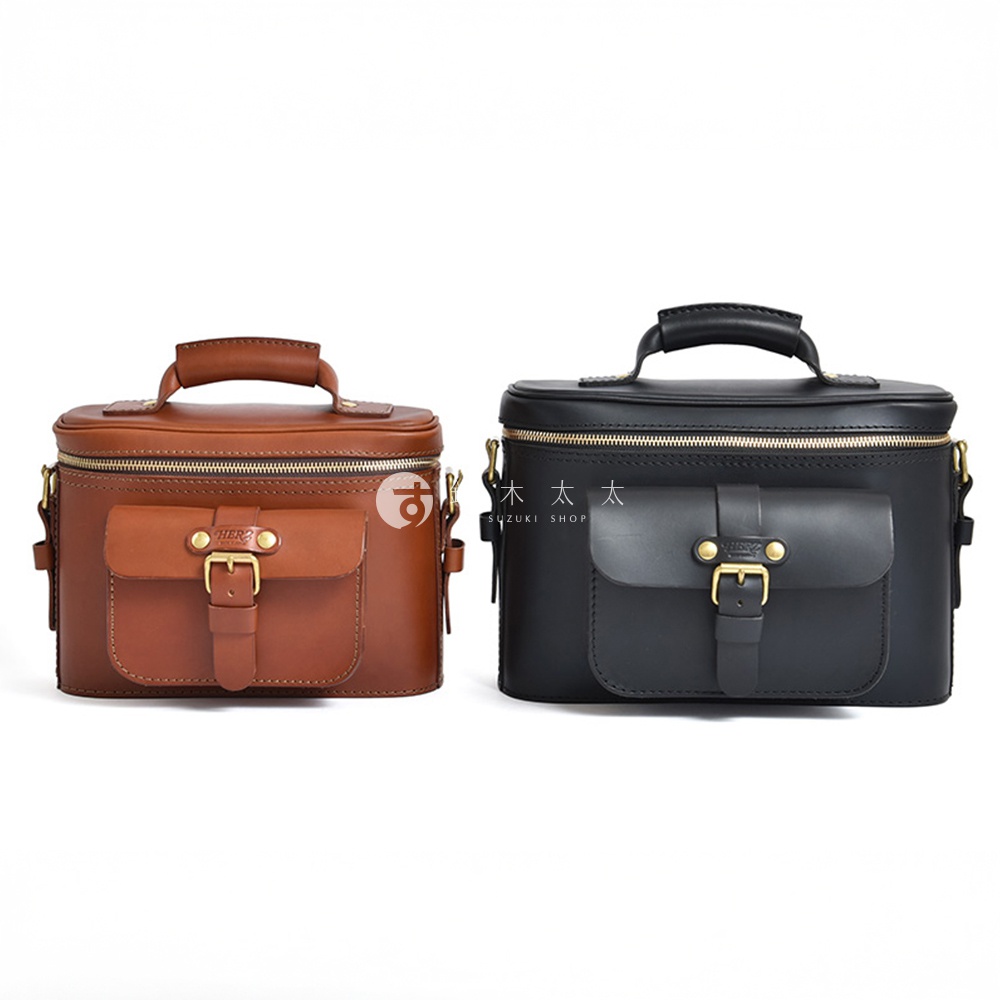 日本HERZ職人手作皮革厚實相機包，一個是褐色，一個是黑色，兩款相機包皆有頂部提把，前方設有翻蓋口袋，並以皮帶和金屬扣環固定。