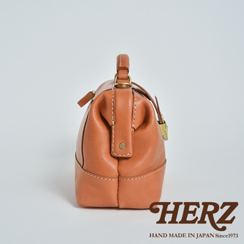 日本HERZ職人手作皮革兩用迷你口金單肩包側面特寫，採用焦糖色Stare皮革製成，呈現硬挺的口金包結構，搭配黃銅五金細節與精緻的手工縫線，包身側面附有品牌標誌。