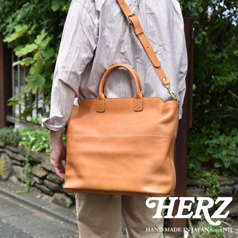 職人手作皮革大容量兩用托特包，呈現溫潤的淺棕色澤，採用光滑皮革材質，搭配雙提把與可拆卸肩帶，整體線條簡潔，適合日常攜帶。