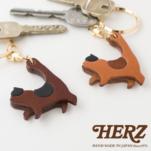 職人手作皮革貓咪造型鑰匙圈，深棕色與淺棕色皮革製成，搭配黑色貓耳與斑點，附有金色鑰匙圈。