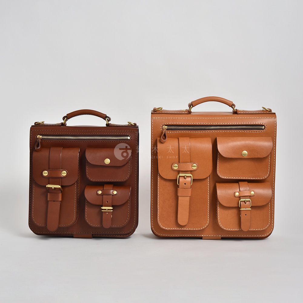 兩款手工皮革後背包，左為深棕色，右為淺棕色，皆為三口袋設計，配有拉鍊與金屬釦環，質感精緻。