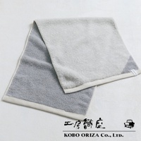 一條棉麻混紡雙色快乾毛巾，左側為灰色，右側為淺灰色，邊緣有白色滾邊。