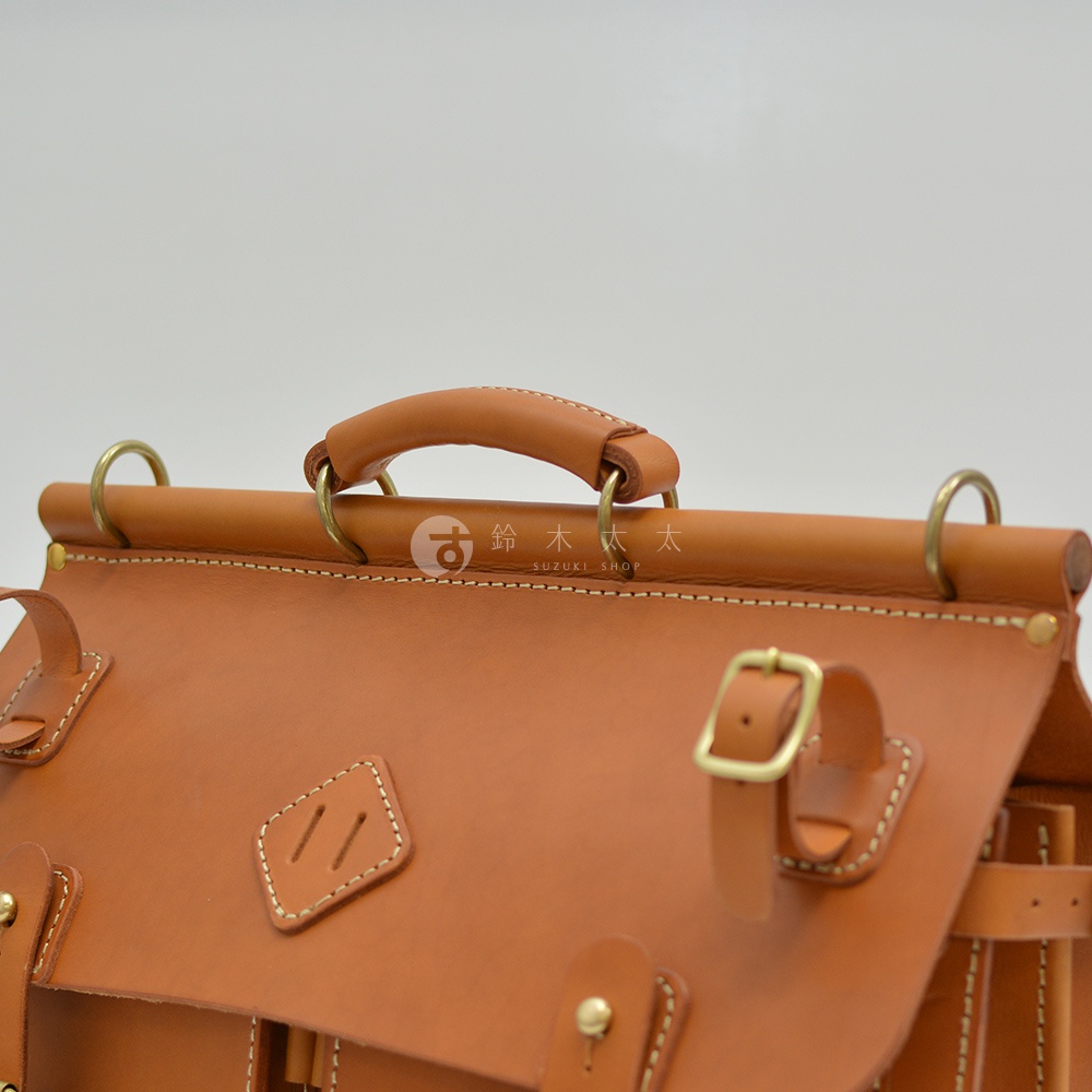 棕色皮革旅行包，設有頂部提把、可調節扣帶和金色金屬配件，展示職人手作質感。