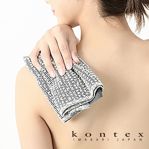 女性手持一條印有黑色條紋圖案的天然素材按摩洗澡巾，放在肩膀上。