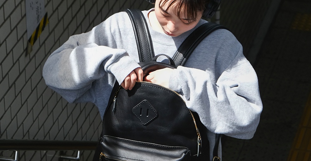 一個黑色皮革休閒風格後背包，具有精緻的縫線細節和一個菱形皮革標誌。背包由高品質皮革製成，配有拉鍊開口。