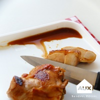 白色防溢迷你砧板上，一塊切好的烤雞肉，旁邊有一把銀色刀。砧板上有深棕色醬汁。