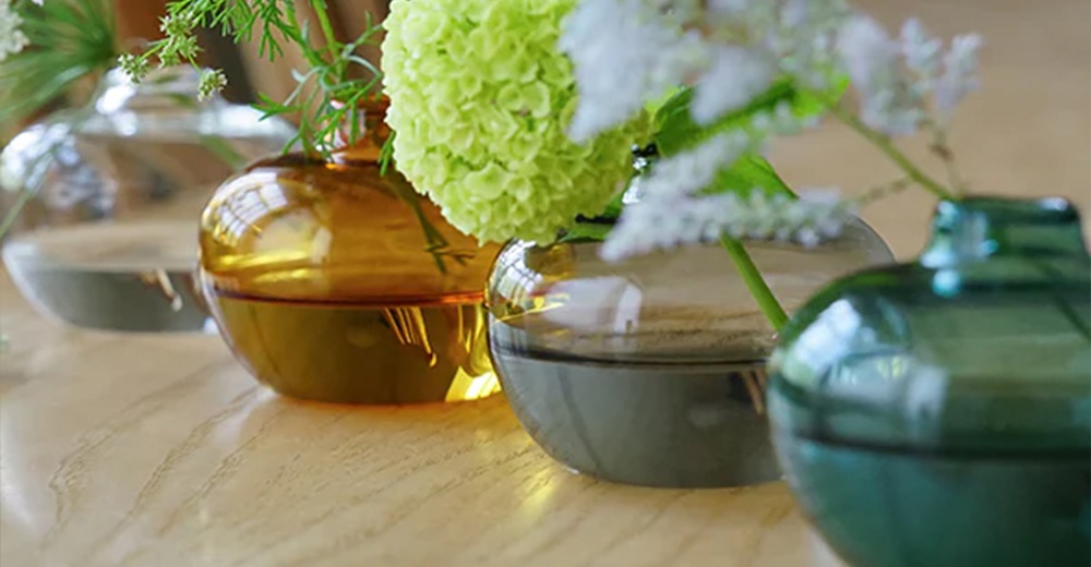 AXCIS Lua 多功能線香玻璃花器，黃色、灰色及綠色玻璃花瓶，搭配綠色和白色花朵，放置於木質桌面。