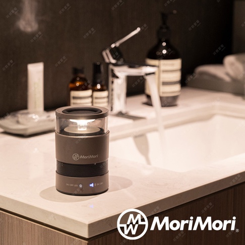 一個深灰色圓柱形無線藍牙音響，頂部有透明燈罩，內有黃色LED燈。音響側面有MoriMori品牌標誌，底部有「ON/OFF LED」和「ON/OFF」按鈕，以及藍牙圖示。