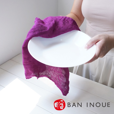 一件紫色三層蚊帳棉織迷你手拭巾，尺寸37x37公分，質地輕柔，用於擦拭白色盤子。