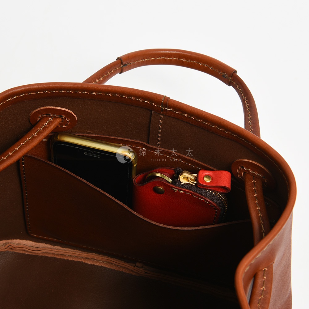 職人手作皮革托特包內部，展示手機和紅色零錢包。