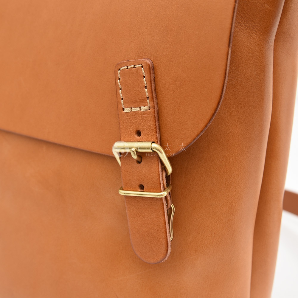 日本HERZ職人手作皮革雙扣旅行郵差包的細節，展示了焦糖色皮革包包上的金色金屬插釦和縫線細節。