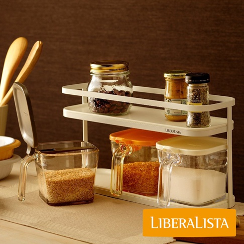 LIBERALISTA 調味料罐收納架組，展示了多款玻璃與塑膠材質的調味料罐，裝有各種食材，架子放置在米黃色桌布上，背景為深棕色。