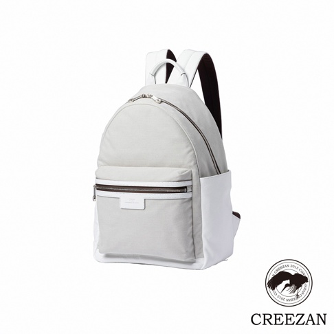 一個簡約風格的CREEZAN品牌後背包，主體採用淺灰色帆布材質，搭配白色皮革飾邊與底部設計，具備頂部提把與前置拉鍊口袋，右下角配有品牌圓形標誌，整體呈現質感優雅的休閒商務風格。