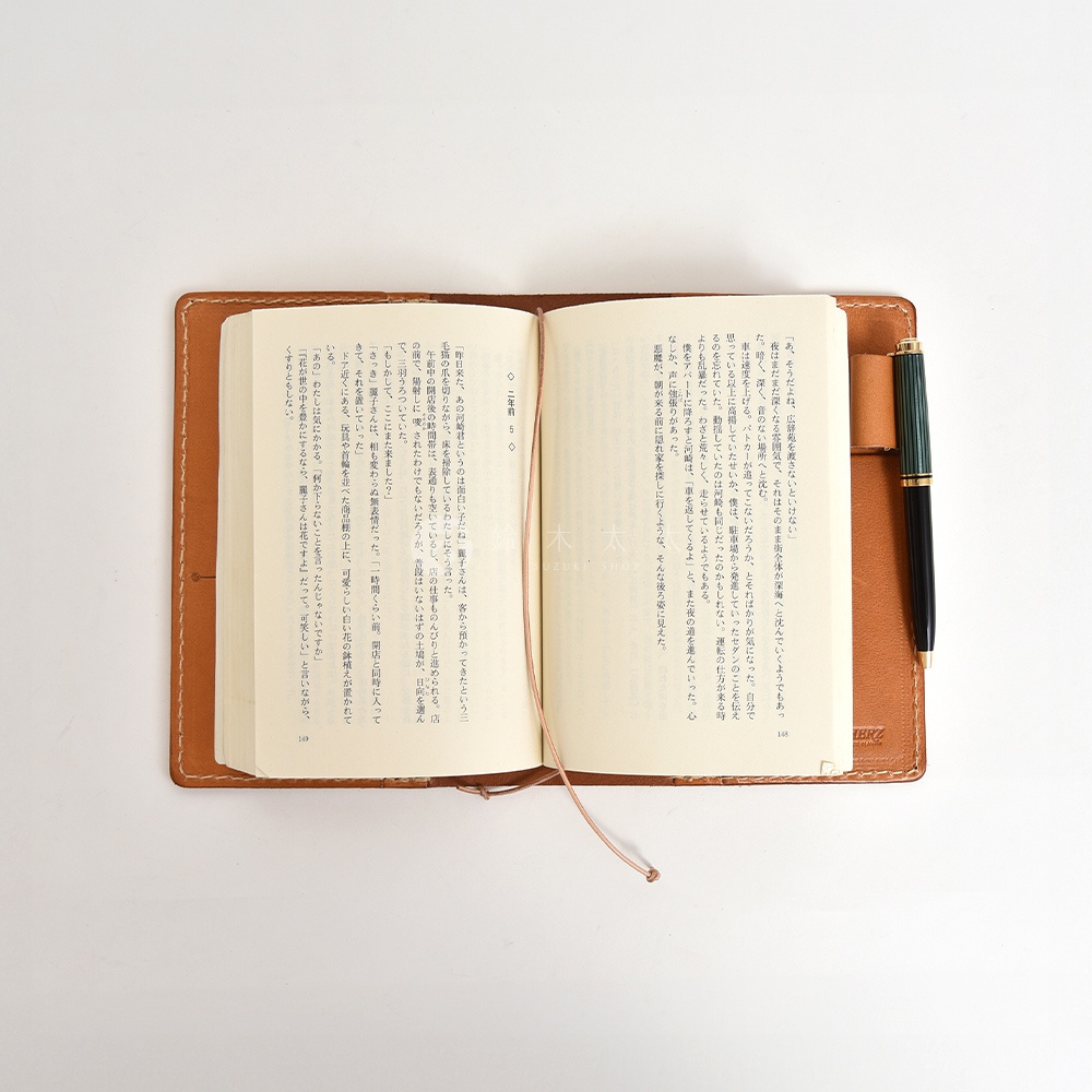 一本皮革手帳書套，打開展示內頁的文字內容，書套旁插著一支筆