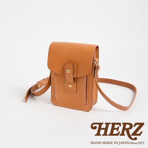 職人手作皮革散步包，原色牛皮材質，方型翻蓋設計，附有金屬釦與皮革束帶，可調節長度的肩背帶。