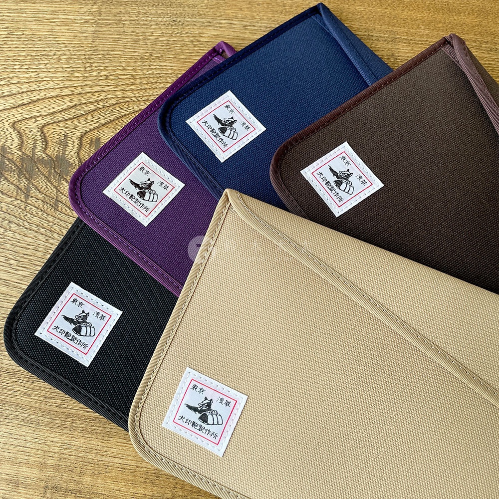 五個犬印純綿帆布平板收納包，顏色有卡其色、黑色、紫色、海軍藍和咖啡色，皆有標示品牌Logo的白色布標。