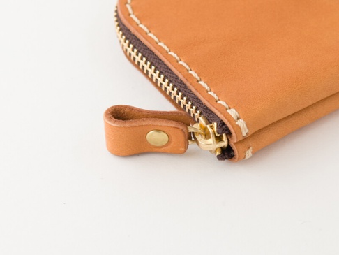 職人手作皮革收納零錢包，採用淺棕色皮革，搭配黃銅色拉鍊和圓形金屬扣。縫線為米白色，呈現細緻的質感。