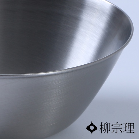 柳宗理品牌的不鏽鋼霧面調理盆局部特寫，金屬表面呈現細緻的拉絲紋理與啞光質感，邊緣線條圓潤流暢，右下角印有標誌性的柳宗理品牌圖示與日文名稱。