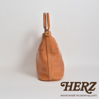 職人手作皮革兩用托特包，經典焦糖棕色，以堅韌的皮革和白色車縫線呈現。包身線條簡潔，配有提把和側邊口袋，展現質感與實用性。