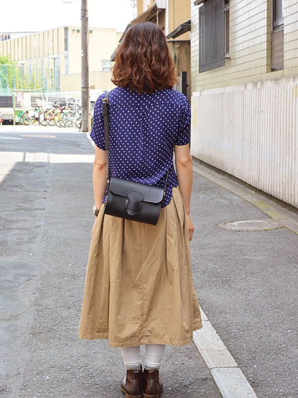 一位女性身穿藍底白點襯衫和卡其色長裙，斜挎一個黑色皮革寬扣帶馬鞍包。