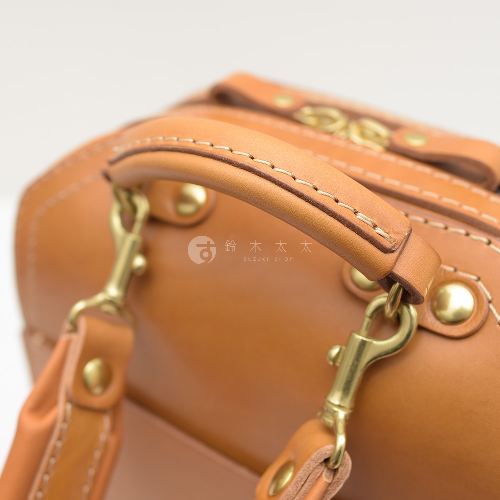 棕褐色皮革手提包，帶有金屬扣環和縫線細節，展現職人手作質感。