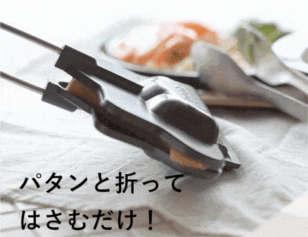 銀色金屬與黑色塑膠材質的熱壓三明治烤夾，夾著一片金黃色的吐司。烤夾由兩支金屬長柄連接，下方鋪著白色布料。