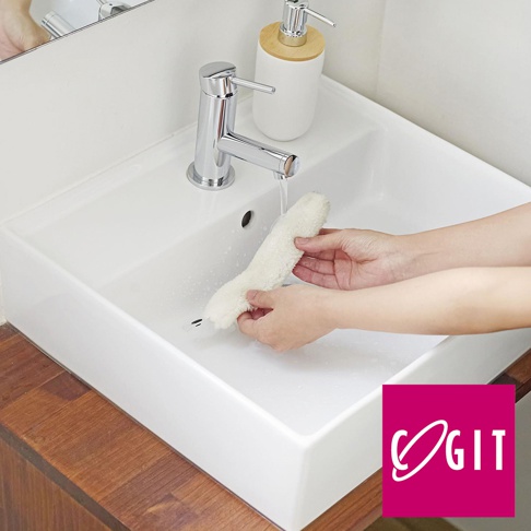 COGIT 品牌的伸縮式冷氣出風口除塵縫隙清潔刷，以粉紅色的方形背景襯托，其中央 logo 包含「COGIT」字樣，圖片展示了雙手正在水龍頭下沖洗一個白色毛絨刷子，置於白色陶瓷洗手台內。