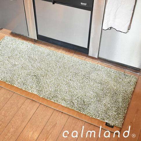 一塊淺綠色的長條形廚房地墊，材質蓬鬆柔軟，帶有天然紋理，放置在木質地板上，旁邊是廚房家電。