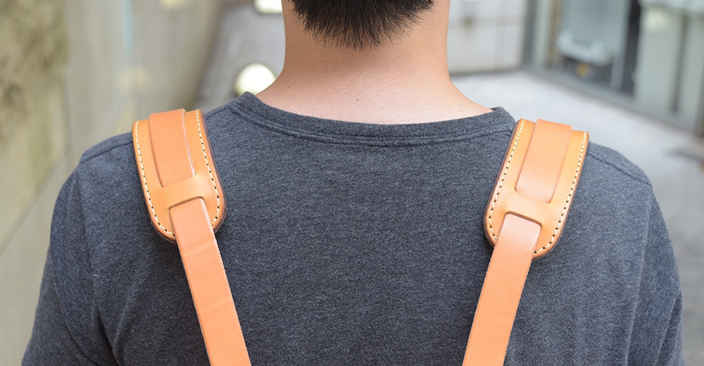 職人手作的淺棕色皮革肩墊，縫線清晰，搭配深灰色上衣，呈現簡約風格。