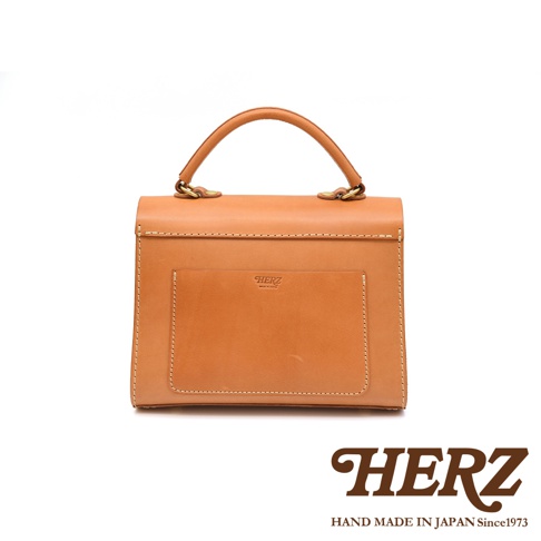 HERZ 焦糖色皮革手提包，正面設有品牌壓印和一個置物袋，搭配金色五金提把。