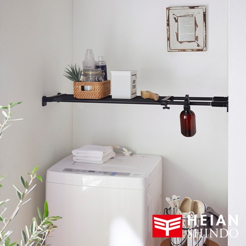 黑色兩段式強化伸縮桿，上方置有洗衣精、籃子、清潔用品等，下方有白色洗衣機及毛巾。